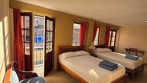 Een kamer met twee houten bedden, een houten bankje en uitzicht buiten door een raam.