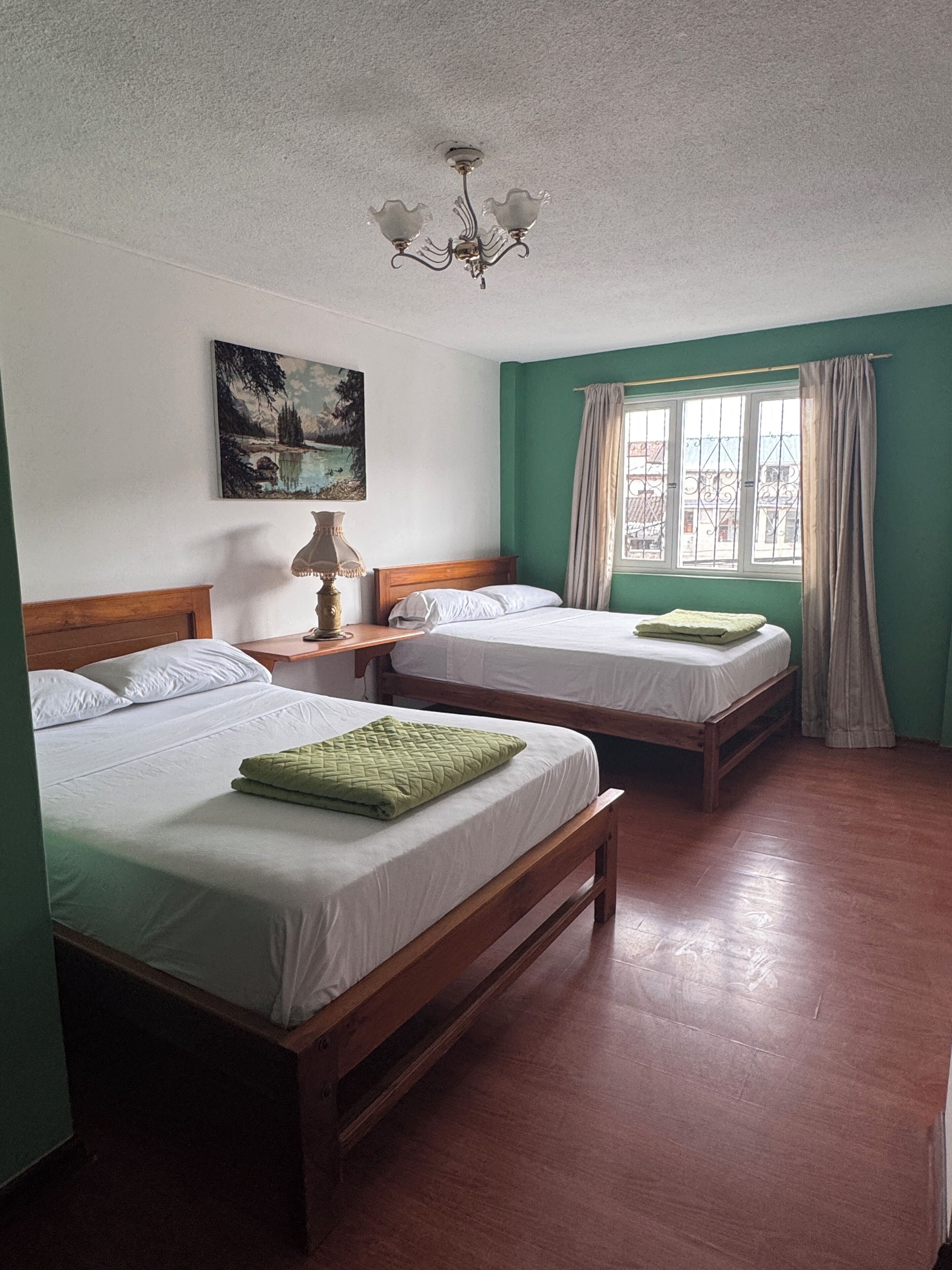 Una habitación con dos camas de madera, un candelabro, un cuadro y una ventana con cortinas.
