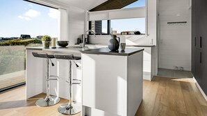 Eine moderne Küche mit einer zentralen Kochinsel, Barhocker und einem großen Fenster mit Blick ins Freie.