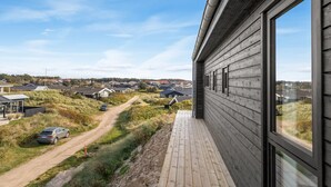Ein modernes Haus mit Holzfassade, einem Balkon und Blick auf ländliche Gegend mit Häusern und einer unbefestigten Straße.