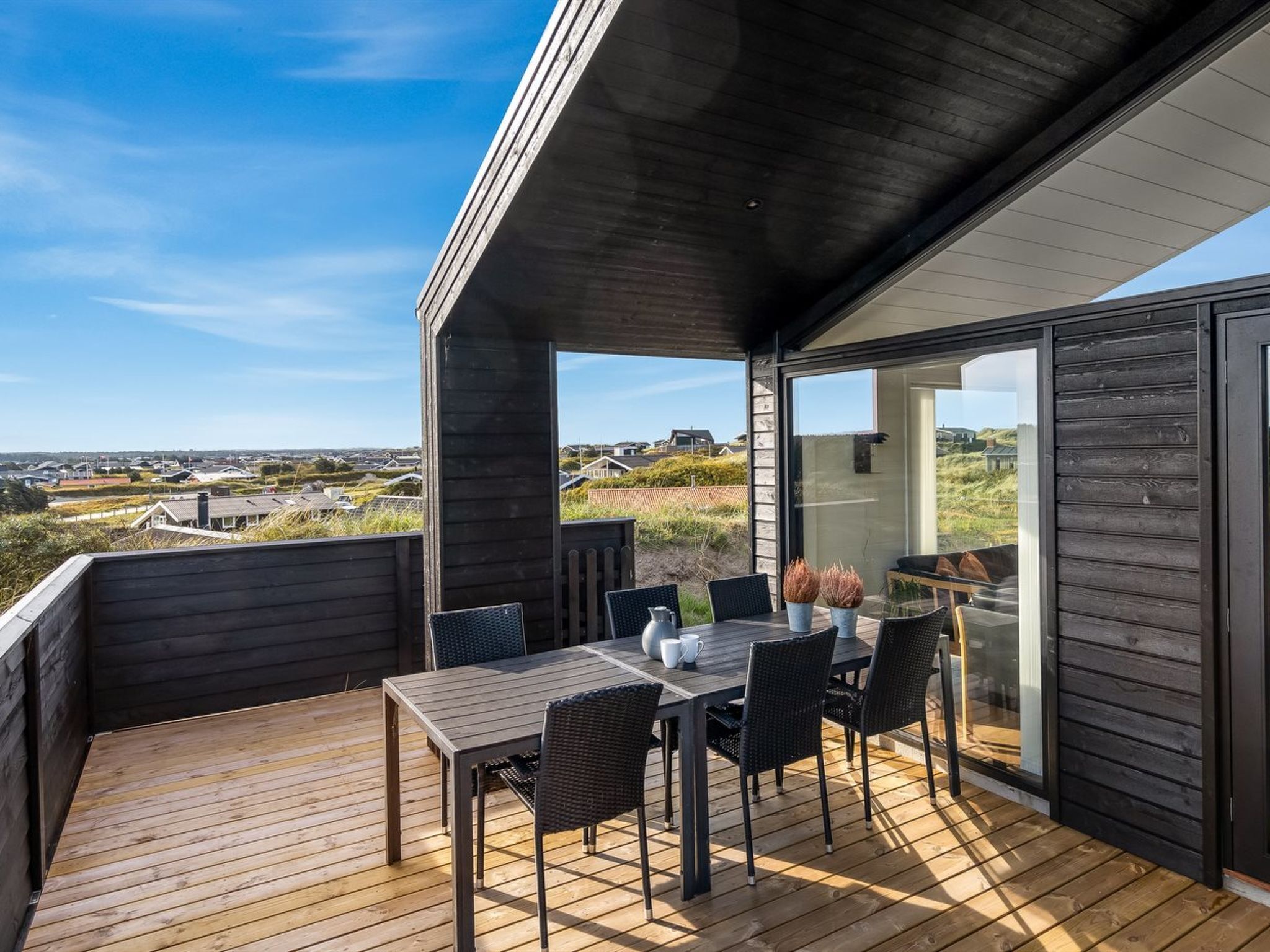 Une terrasse en bois avec une table et des chaises, offrant une vue sur un paysage côtier.