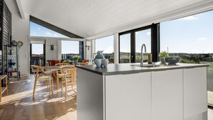 Eine moderne Küche mit einer großen Kochinsel, Holzböden und großen Fenstern mit Blick ins Grüne.
