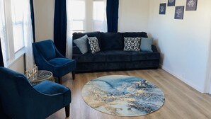 Ett vardagsrum med en mörkblå soffa, två likadana fåtöljer, ett runt soffbord och en lampa med flätad skärm.