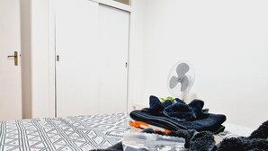 Ein Bett mit einem gemusterten Bettüberwurf, ein Ventilator und ein Stapel gefalteter Kleidung auf einem Nachttisch.