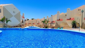 Ein Swimmingpool mit klarem, blauem Wasser, umgeben von Gebäuden mit roten Ziegeldächern und beigen Fassaden.