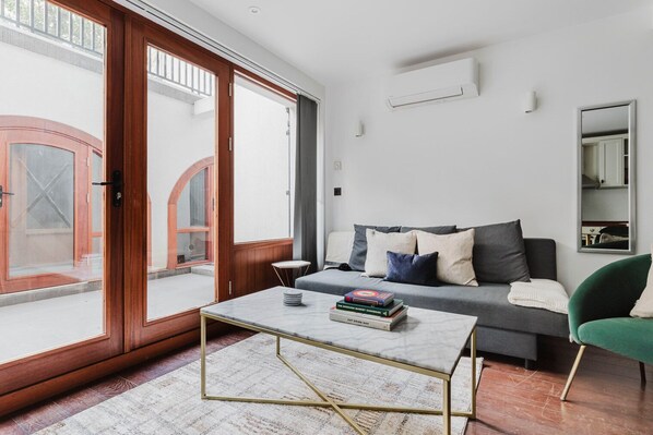 A modern living room with a grey sofa, a coffee table, and a green armchair. There is a sliding glass door leading to an outdoor area. - Chic Fitzrovia 1BR, Furnished & Equipped, by Blueground (London)