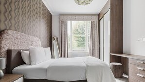 A bedroom with a bed, bedside table, dresser, and a window with curtains. - Cool Notting Hill 1BR, Fully Furnished & Ready, by Blueground (London)