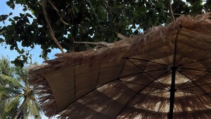A beachside setting with thatched umbrellas, a green boat, and a calm sea. - The Bangka Place (Enrique Villanueva)