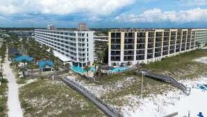 Ein Strandhotel mit mehreren Etagen, einem Schwimmbad und einer Promenade, die zum Strand führt.