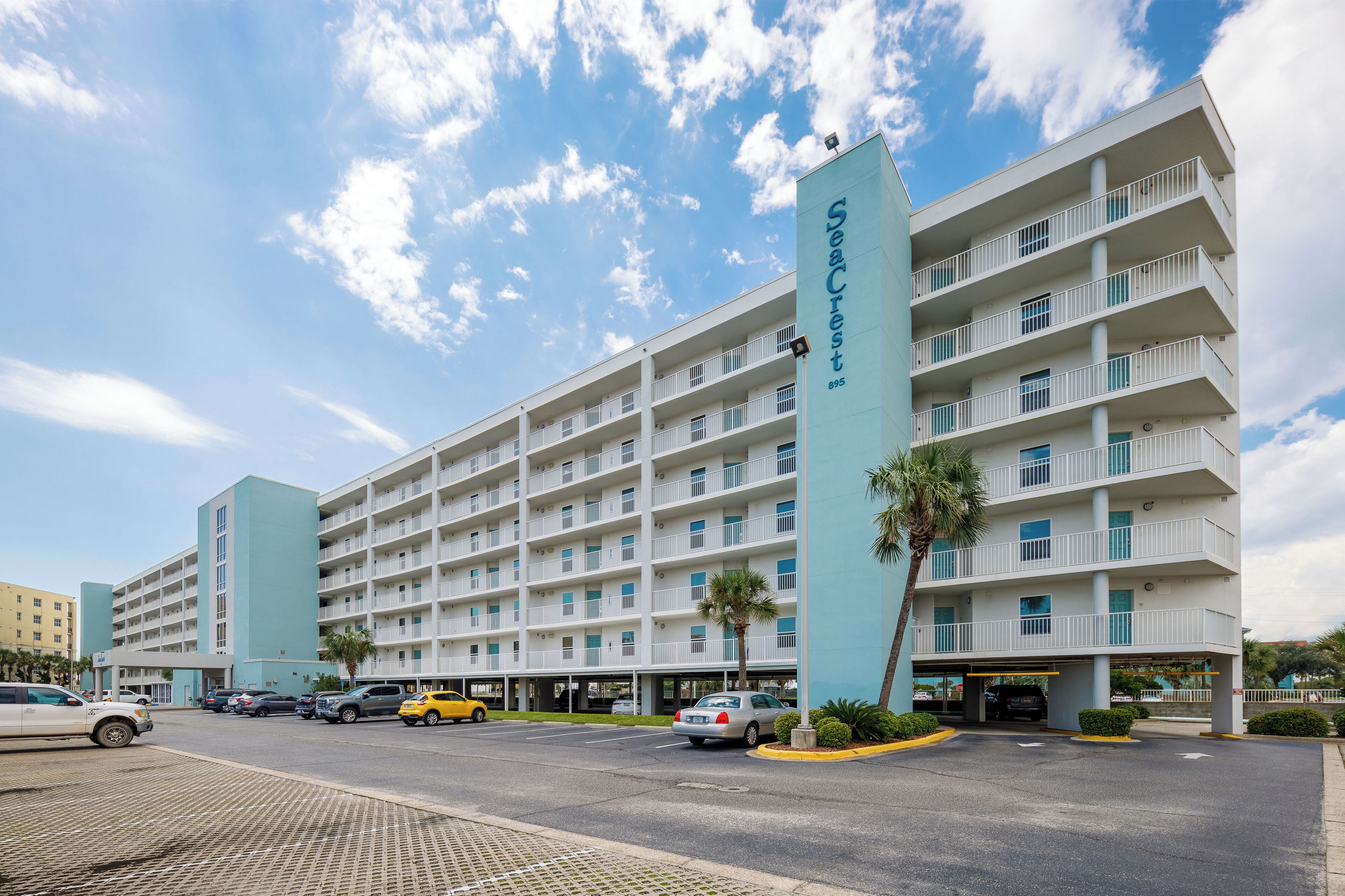 A multi-story hotel with a prominent 'SeaCrest' sign, multiple balconies, and a parking area with several cars.