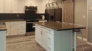Una cocina moderna con armarios blancos, una isla central con taburetes y una campana extractora de acero inoxidable, además de un salpicadero oscuro.