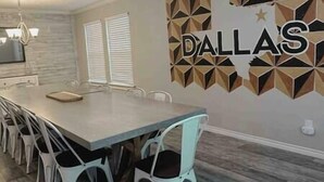 Un comedor con una mesa larga, sillas blancas y una decoración en la pared con la palabra "DALLAS".