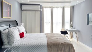 A modern bedroom with a large bed, a desk, and an air conditioning unit. - Gated 1-bedroom Condo in Portmore with AC, WiFi, Pool, Kitchen, TV, Beach View (Portmore)