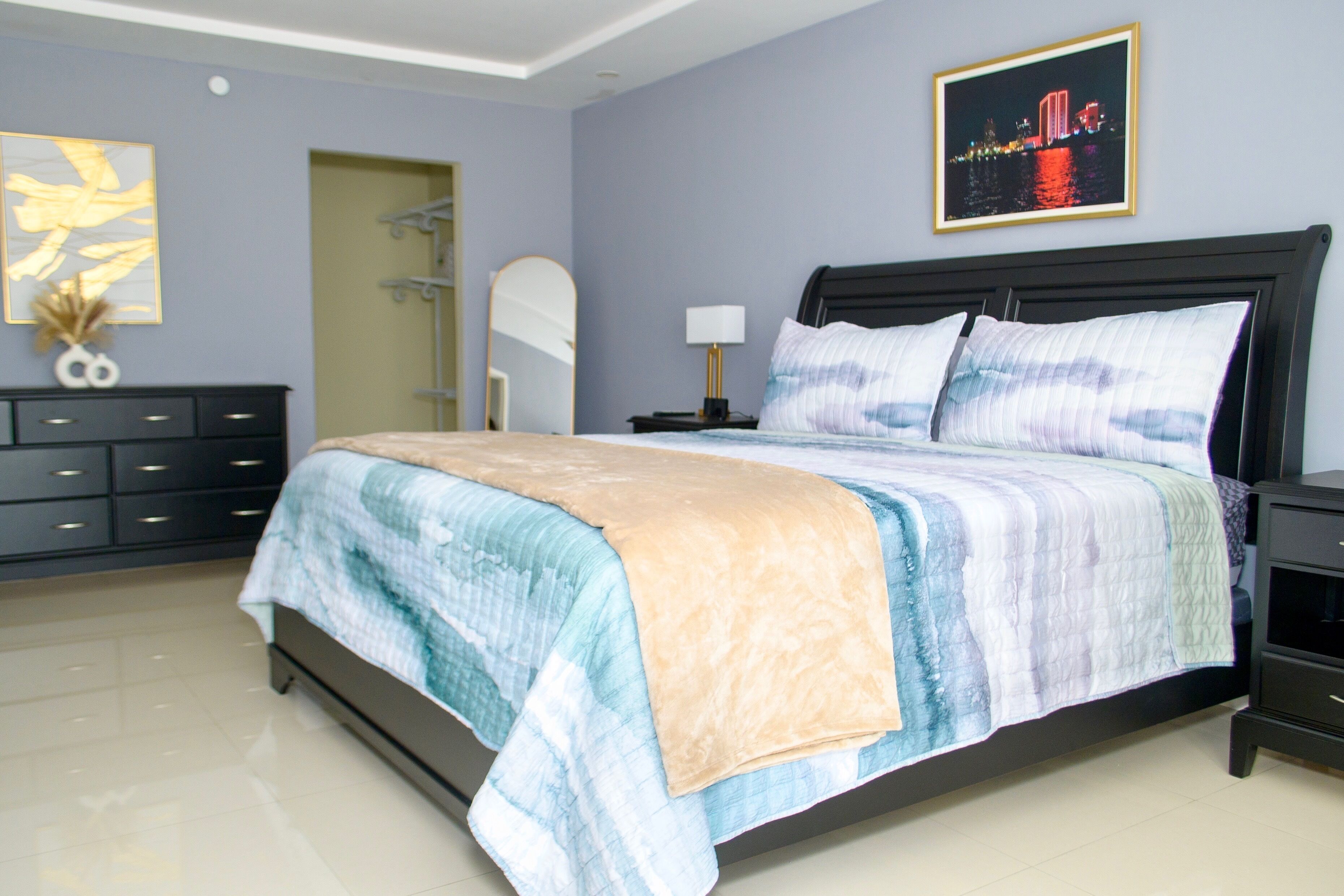 Quarto com cama, mesas de cabeceira, cômoda, espelho e um quadro na parede.