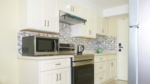 A kitchen with white cabinets, a microwave, a stove, and a tiled backsplash. - Gated 1-bedroom Condo in Portmore with AC, WiFi, Pool, Kitchen, TV, Beach View (Portmore)
