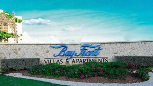 A sign for Bay Front Villas & Apartments with a stone wall and a landscaped area with flowers. - Gated 1-bedroom Condo in Portmore with AC, WiFi, Pool, Kitchen, TV, Beach View (Portmore)
