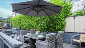 Un patio al aire libre con mobiliario de mimbre, una mesa de vidrio y una sombrilla.