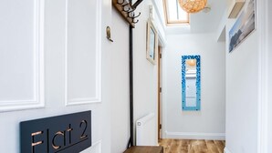Un pasillo con suelo de madera, paredes blancas, una puerta con la etiqueta 'Flat 2' y una ventana con marco azul.