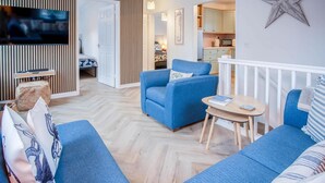 Una sala de estar moderna con sofás azules, una pequeña mesa de madera y un televisor.