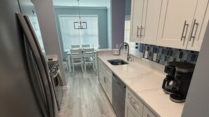 A modern kitchen with a built-in oven, a dishwasher, a coffee maker, and a dining area with a table and chairs. - Modern & Clean, Family Friendly, 1st Floor Condo (Rehoboth Beach)