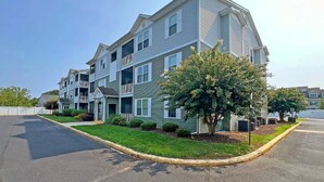 A multi-story residential building with a green exterior, multiple balconies, and a well-maintained lawn. - Modern & Clean, Family Friendly, 1st Floor Condo (Rehoboth Beach)