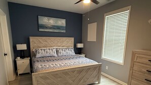 A bedroom with a bed, nightstands, a dresser, a ceiling fan, a window with blinds, and a painting on the wall. - Modern & Clean, Family Friendly, 1st Floor Condo (Rehoboth Beach)