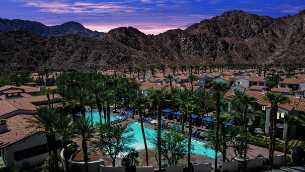 A resort with a pool surrounded by palm trees and mountain views.