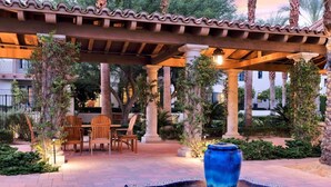 A covered outdoor seating area with a fountain, chairs, and a pergola.