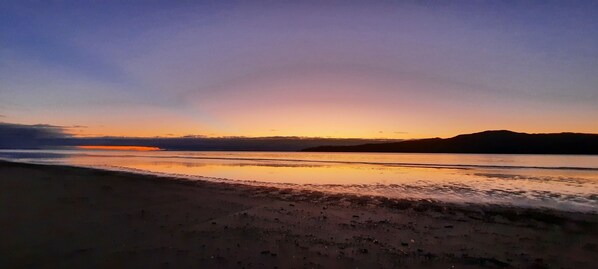 A beach at sunset with calm waters reflecting the sky.
