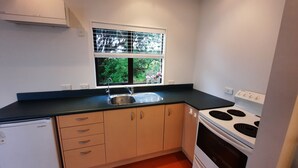 A compact kitchen with a built-in dishwasher, a stove, and a window with blinds. - Sunset cottage Paekākāriki - sand, sea and sunsets (Paekakariki)