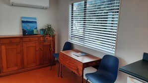 A room with a wooden desk, a chair, a window with blinds, a cabinet, and a painting on the wall. - Sunset cottage Paekākāriki - sand, sea and sunsets (Paekakariki)