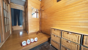Ein Flur mit Holzwänden, einem Spiegel und einem hölzernen Kleiderständer. Auf einem Schrank stehen Körbe und am Boden ein Paar Hausschuhe.