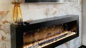 A modern living room with a flat-screen TV mounted on a marble wall, a black entertainment unit with a built-in fireplace, and a decorative vase with dried flowers. - Cozy apartment in Monteserrin! (Quito)