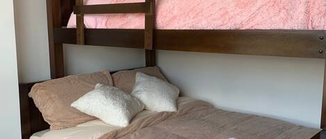 Een stapelbed met een onderbed en een bovenbed, beide met roze beddengoed. Er liggen kussens op het onderbed en een opgerolde handdoek op het bovenbed.