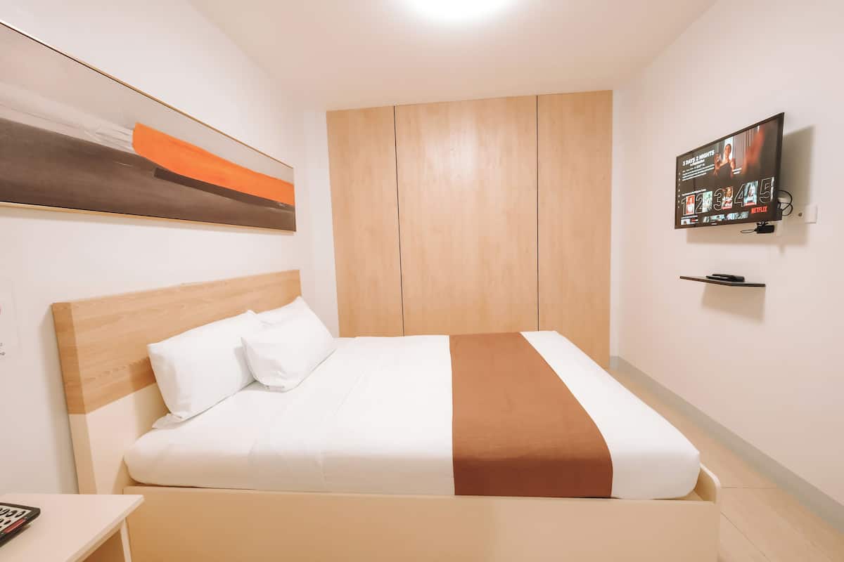 Habitación de hotel con una cama, un televisor montado en la pared y un armario de madera.
