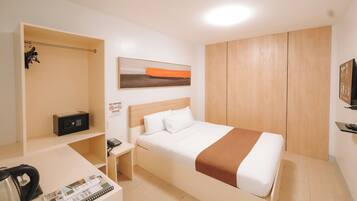 A hotel room with a bed, a desk with a chair, a wardrobe, and a TV on a stand.