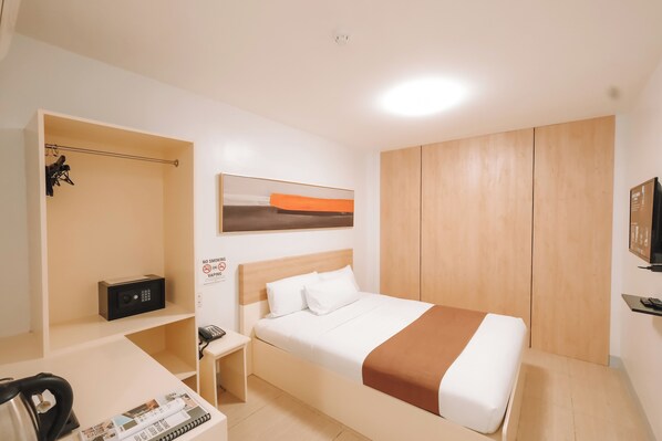 A hotel room with a bed, a desk with a chair, a wardrobe, and a TV on a stand. - Rosey Hotel (Cabanatuan)