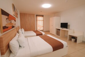 A hotel room with two beds, a desk, a TV, and a wardrobe. - Rosey Hotel (Cabanatuan)