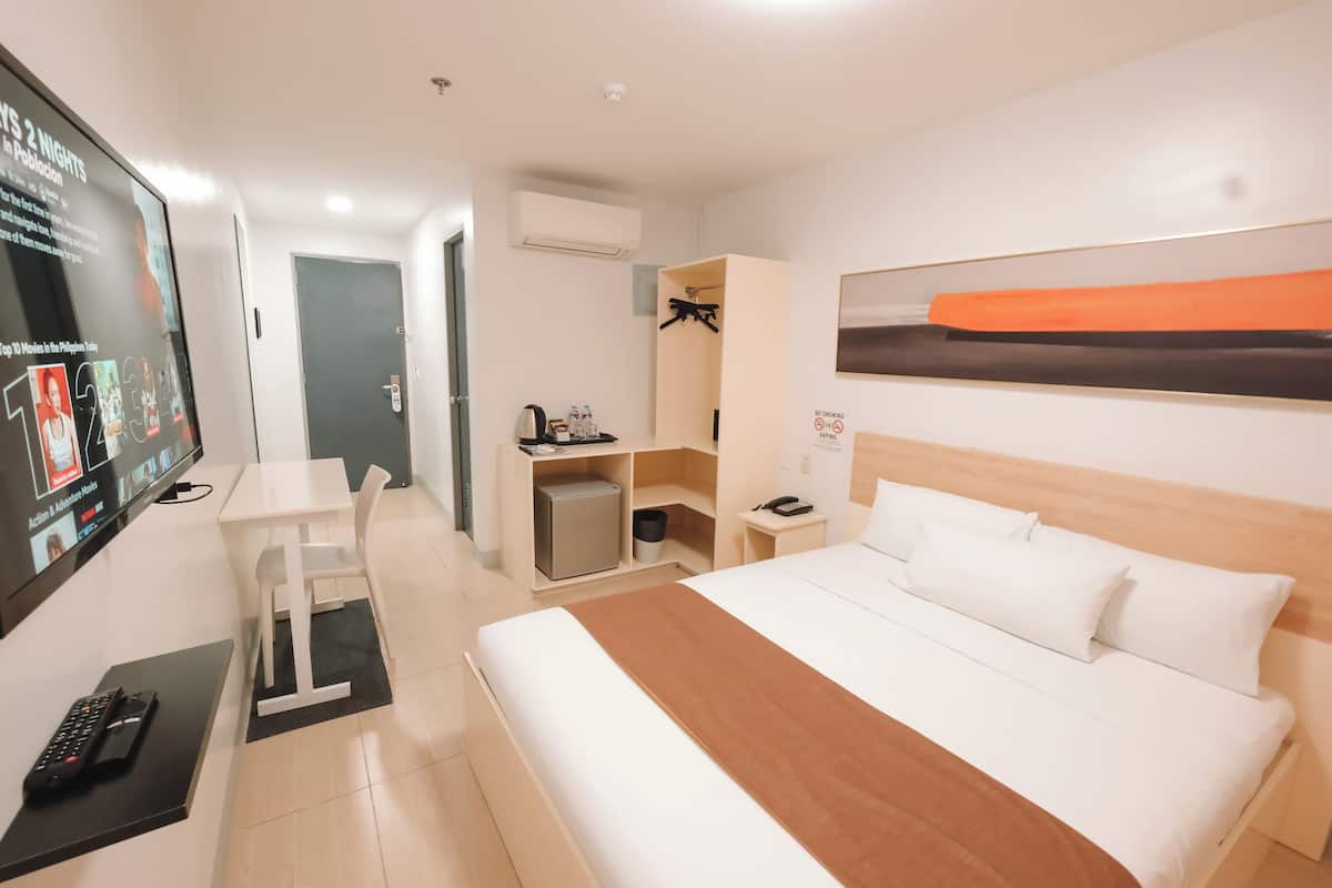Una habitación de hotel con cama, escritorio, silla, televisor y armario.