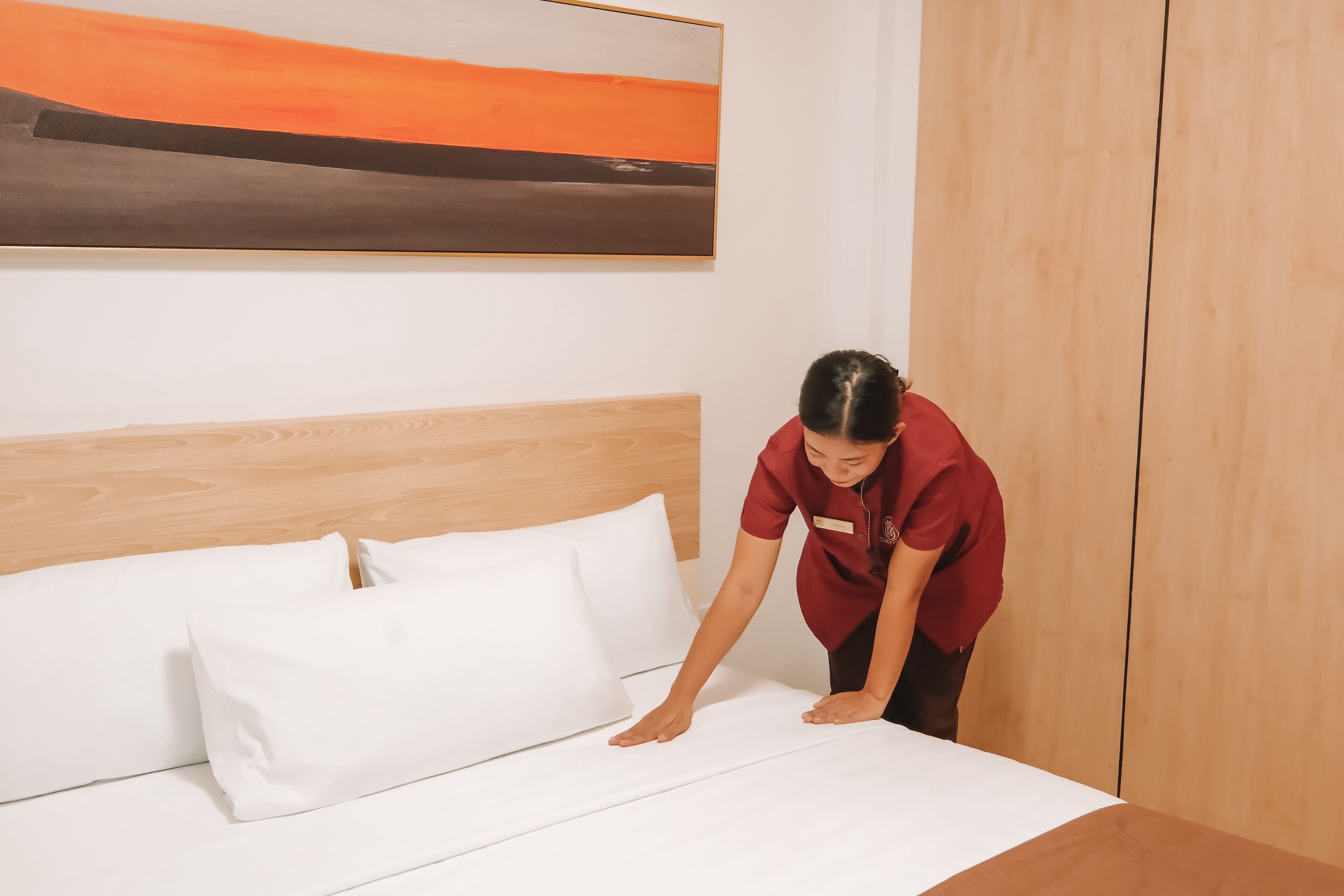 Una cama bien hecha con sábanas y almohadas blancas, en una habitación con cabecera de madera y un cuadro en la pared.