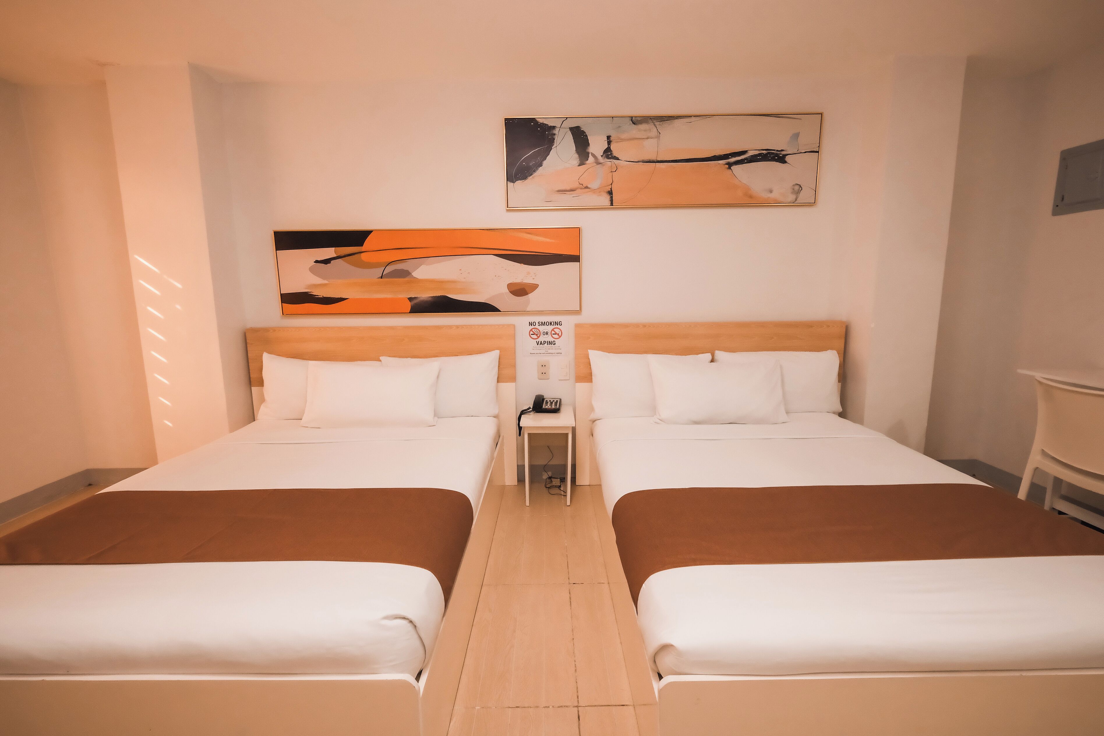 A hotel room with two beds, a nightstand, and a wall-mounted artwork.