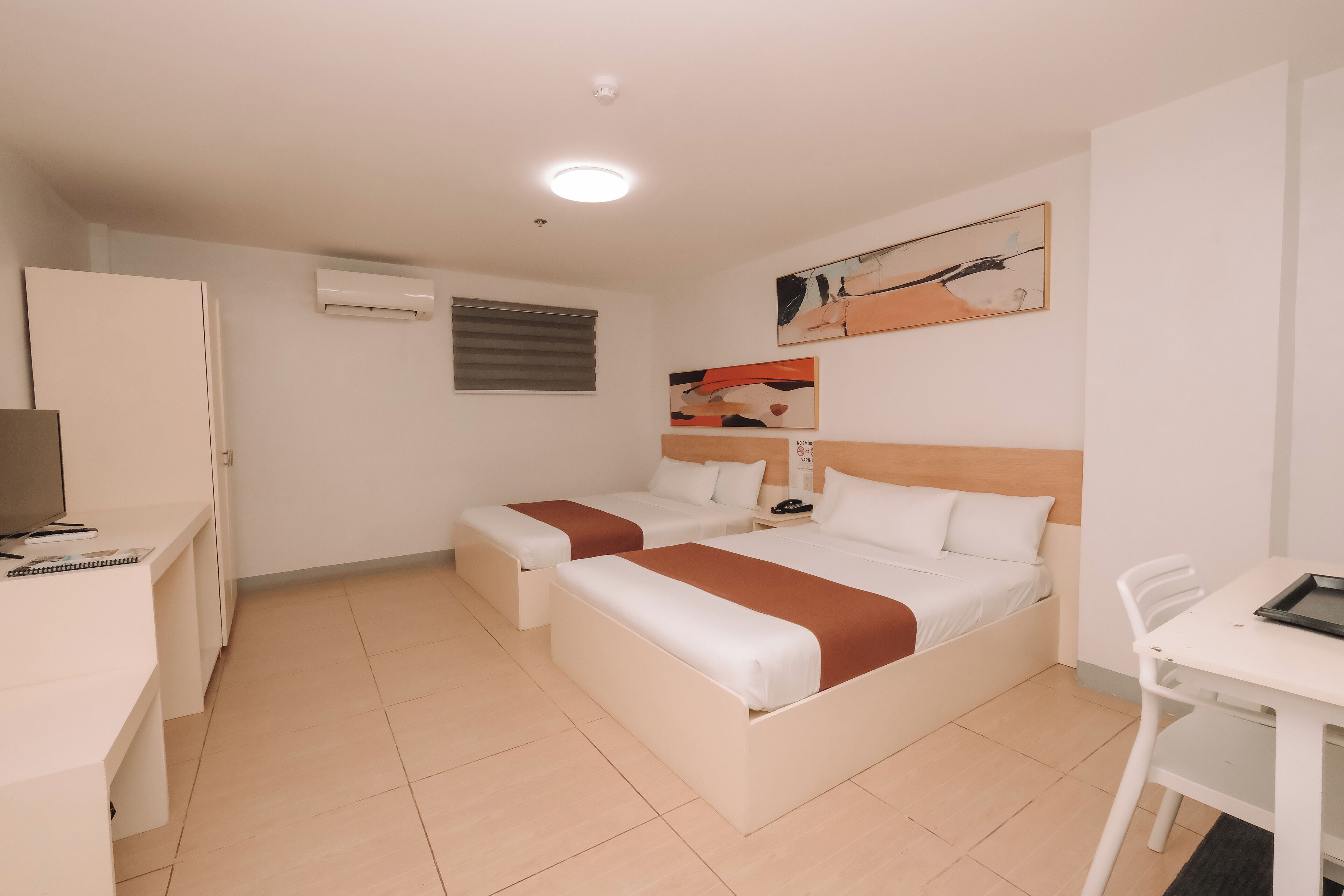 A hotel room with two beds, a desk, a chair, and a TV.