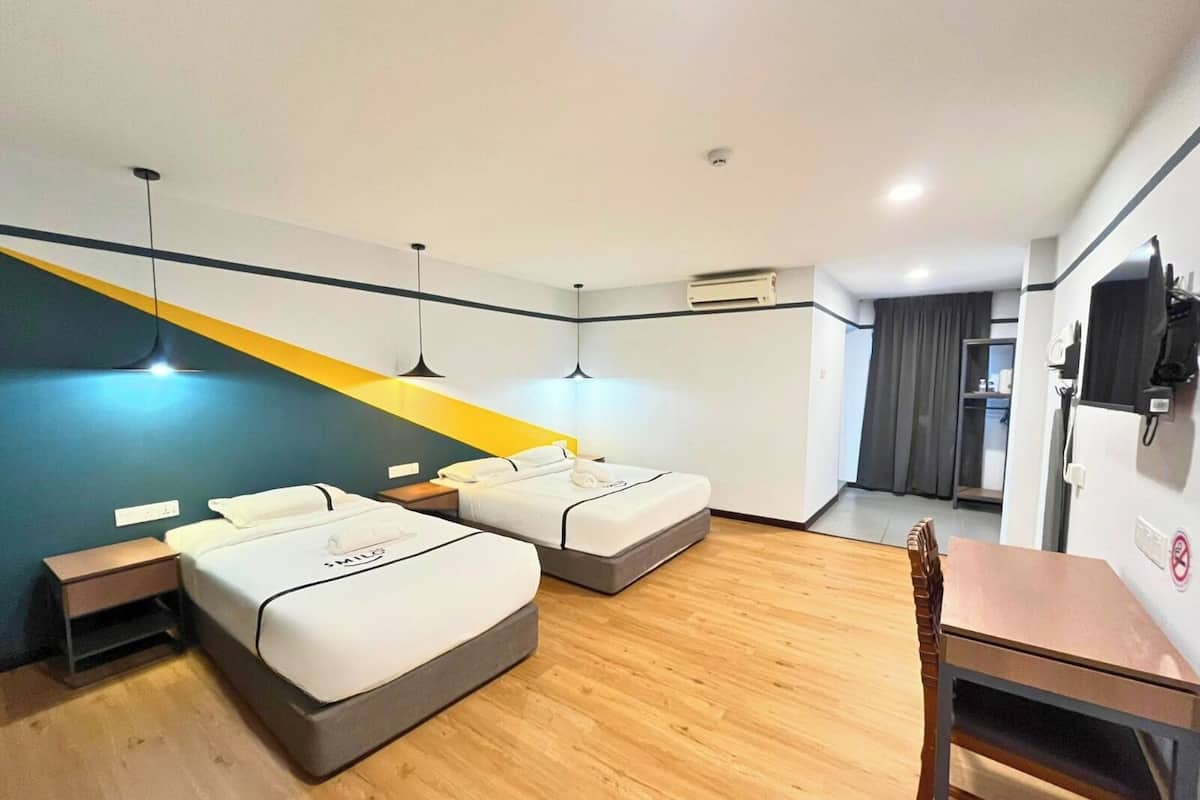 Une chambre d’hôtel avec deux lits, un bureau et une chaise. On y trouve une petite table et une étagère sur laquelle sont posés divers objets.