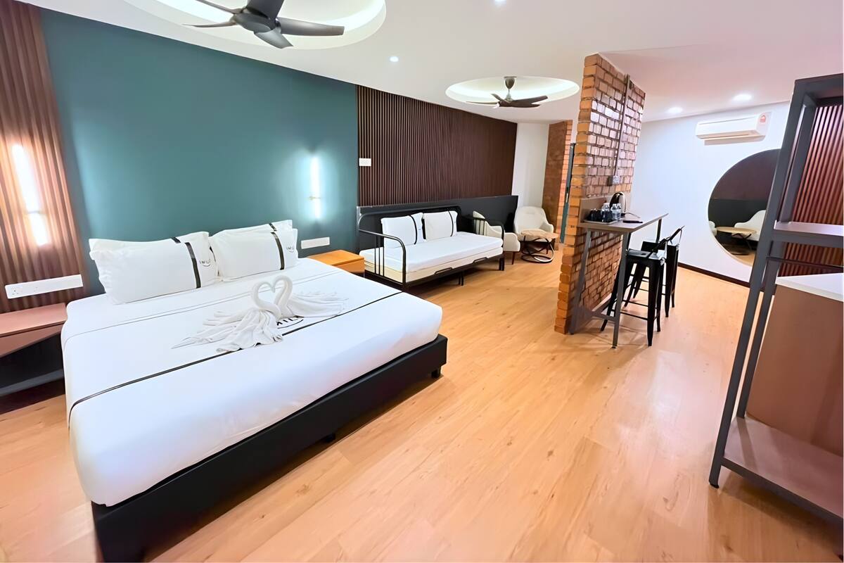 Une chambre d’hôtel moderne avec un grand lit, deux petits lits, un bureau et un espace salon circulaire.