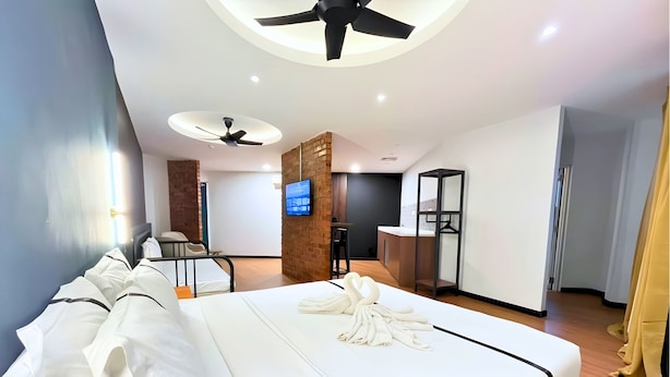 Ein modernes Hotelzimmer mit einem großen Bett, zwei Deckenventilatoren, einem Fernseher und einer kleinen Küchenzeile.