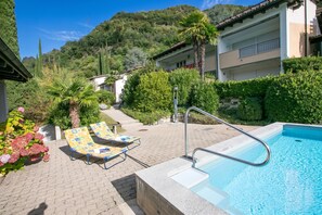 Un área de piscina con sillas de descanso, una terraza junto a la piscina y montañas al fondo.
