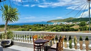 Un balcon avec vue sur la mer, un palmier et une balustrade blanche.