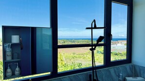 Un baño con un ventanal amplio, un dispensador de toallas y un estante con artículos de aseo.