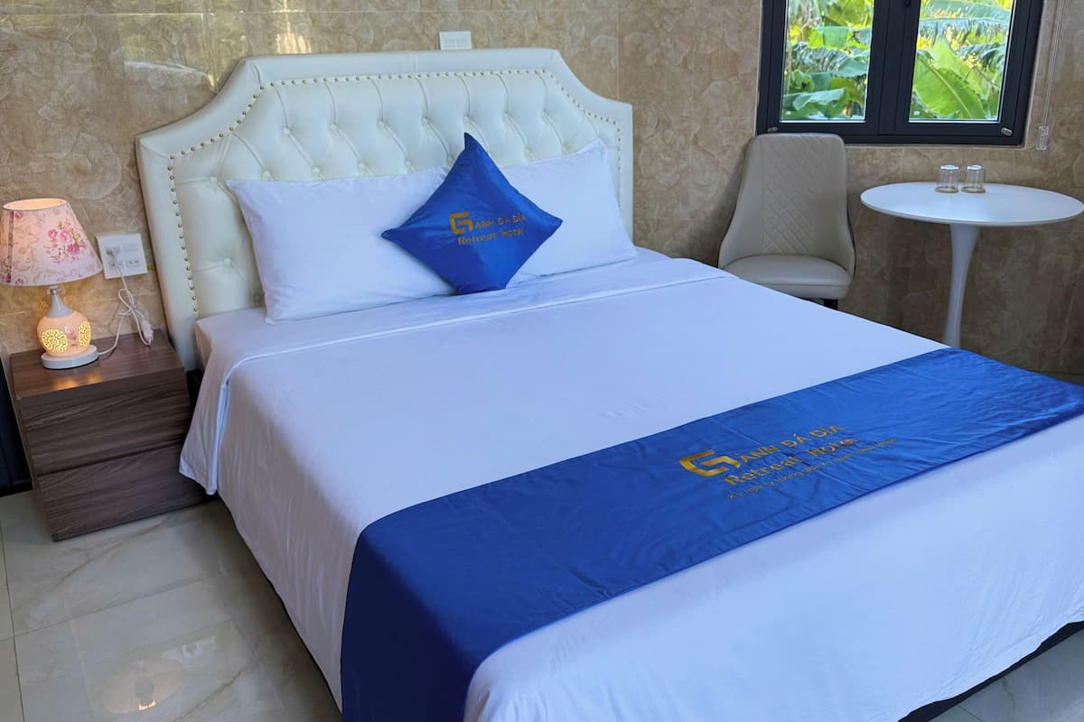 A hotel room with a large bed, a nightstand with a lamp, a chair, and a small table.