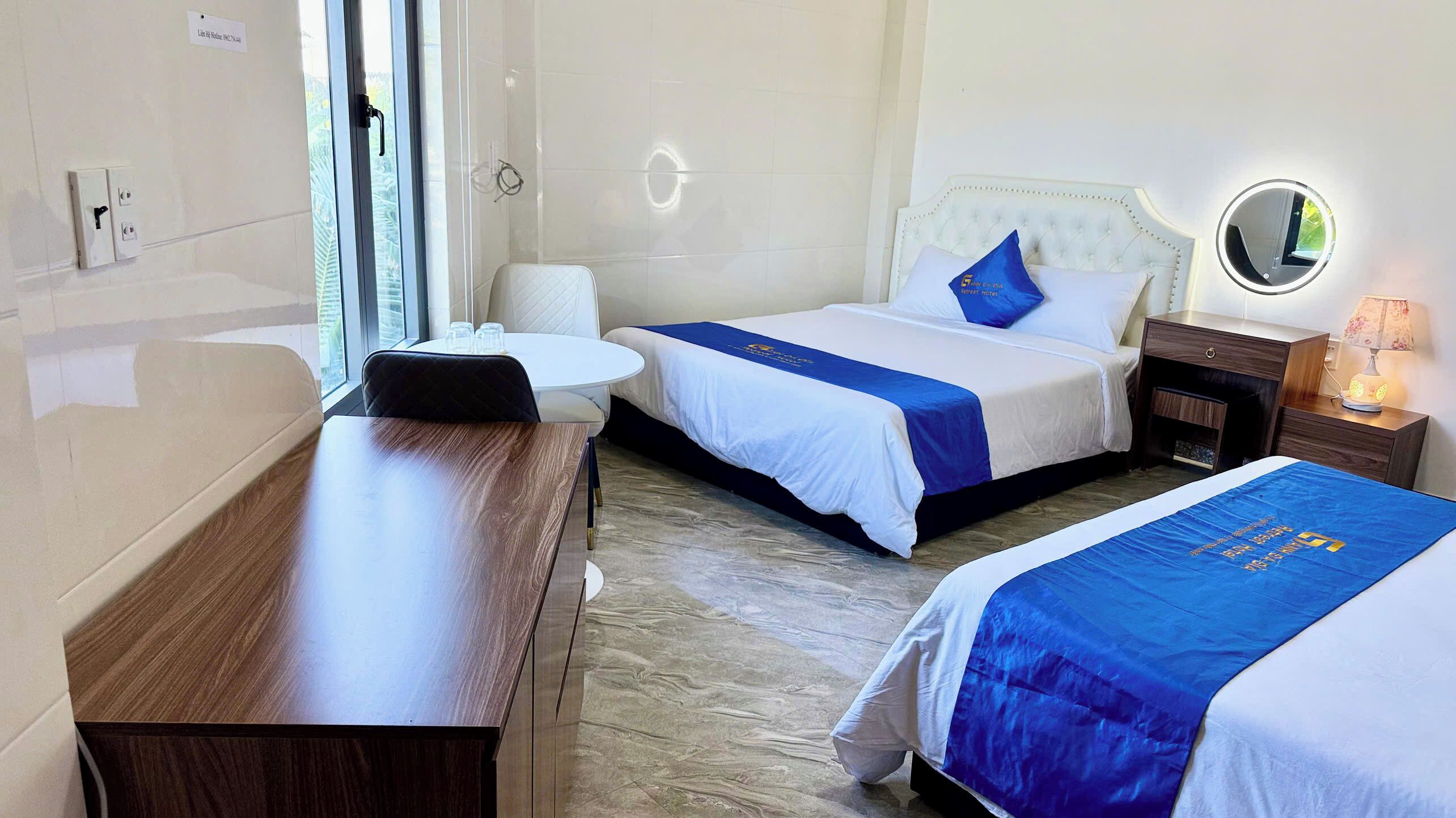 Une chambre d’hôtel avec deux lits, un bureau, une chaise, un miroir rond et une table de chevet.